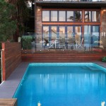 Closer shot of a pool next to a house and a wall made out of wood