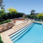 A modern pool with descending steps along the way surrounded by a garden